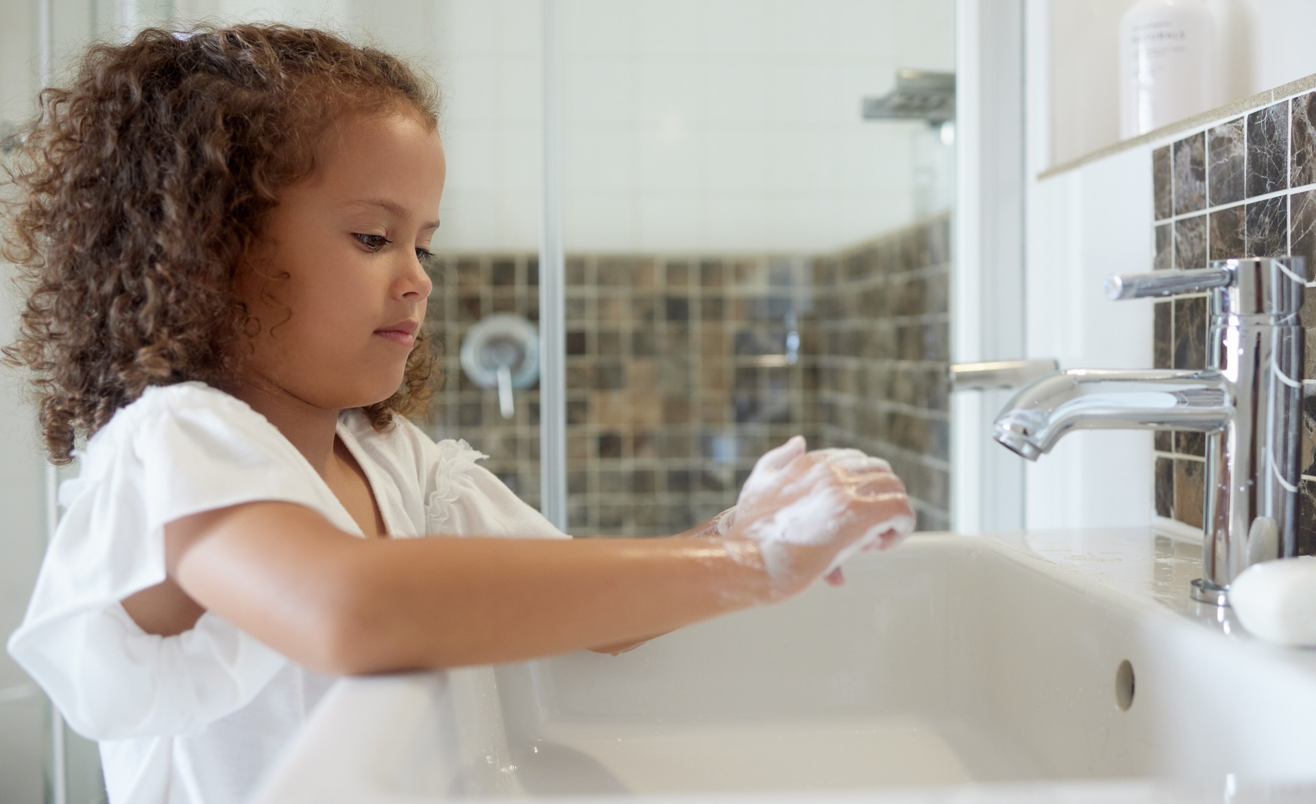 Little girl washing hands with water and soap in bathroom at home. Learning about and practicing good hygiene  keeps us healthy. Child cleaning fingers at a basin or sink